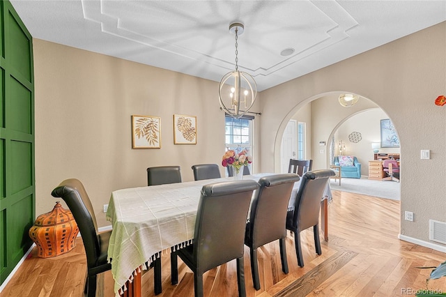 dining space featuring arched walkways, parquet floors, a chandelier, baseboards, and visible vents