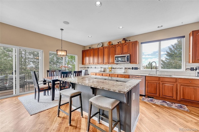 kitchen with brown cabinets, appliances with stainless steel finishes, a sink, light wood finished floors, and tasteful backsplash