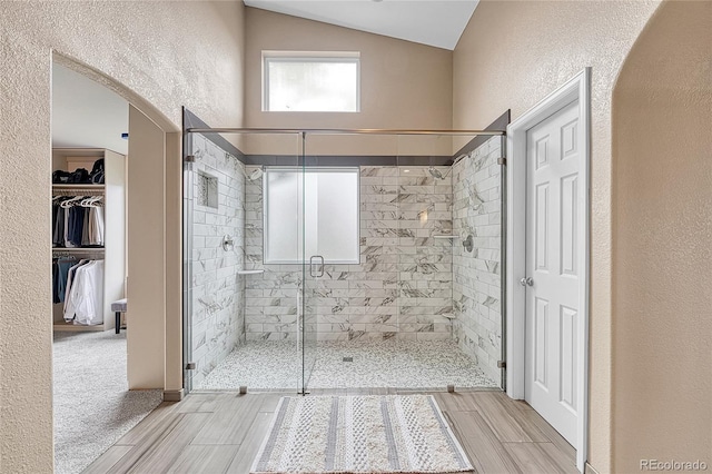 bathroom featuring a textured wall, wood finished floors, a walk in closet, high vaulted ceiling, and a shower stall