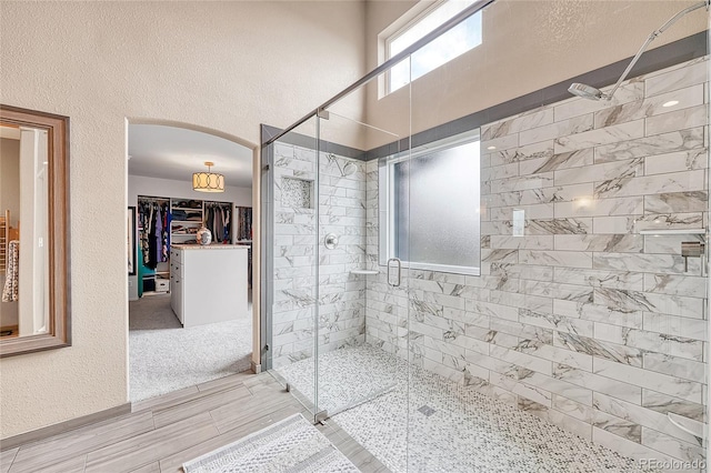 full bathroom with a walk in closet, a textured wall, and a stall shower