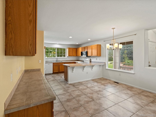 386 Monte Vista St, Brighton, CO 80601 - kitchen featuring white appliances, a peninsula, a chandelier, a kitchen breakfast bar, and light countertops