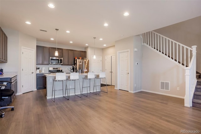 kitchen featuring a kitchen breakfast bar, wood-type flooring, pendant lighting, a center island with sink, and stainless steel appliances