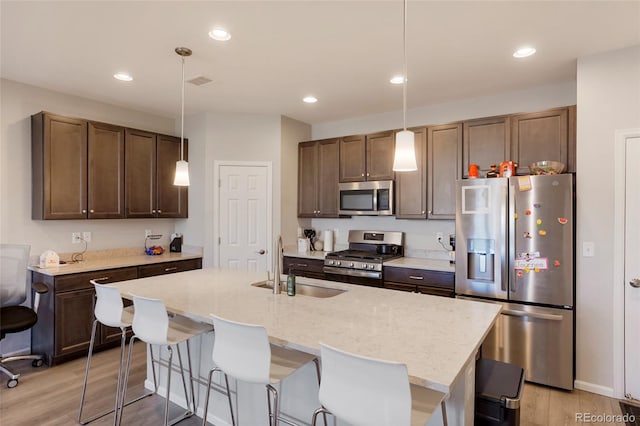 kitchen with hanging light fixtures, a center island with sink, appliances with stainless steel finishes, and a sink