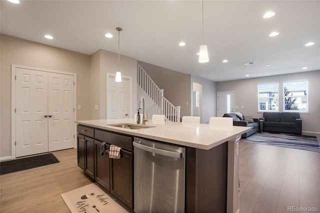 kitchen with pendant lighting, dark brown cabinetry, sink, stainless steel dishwasher, and a center island with sink