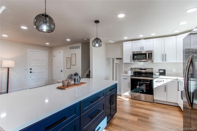 kitchen featuring stainless steel appliances, visible vents, white cabinetry, light wood finished floors, and decorative light fixtures