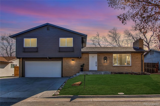 tri-level home with brick siding, a chimney, concrete driveway, a lawn, and fence