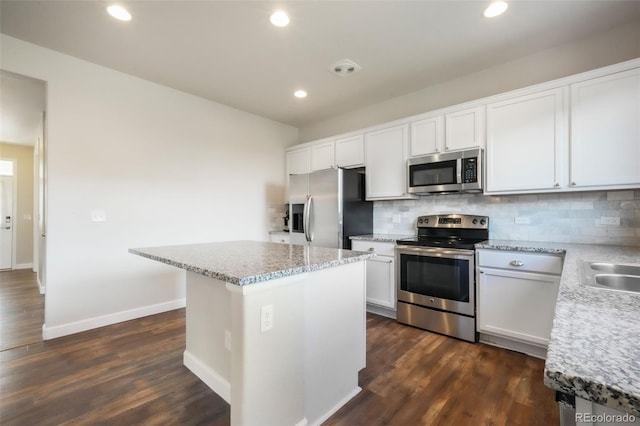 kitchen with stainless steel appliances, light stone countertops, decorative backsplash, and a center island