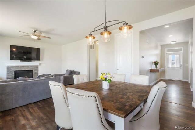 dining area featuring baseboards, ceiling fan, dark wood-style flooring, and a stone fireplace