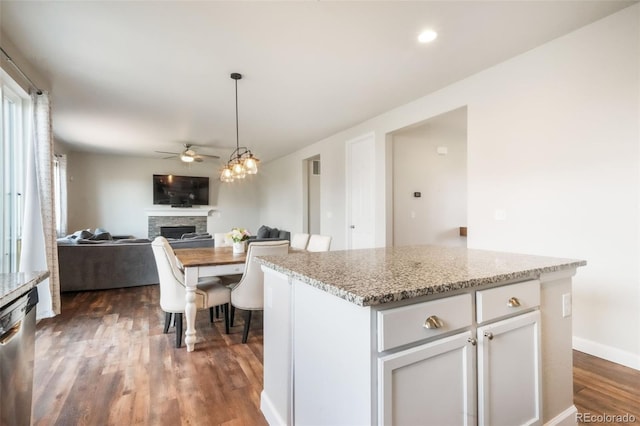 kitchen featuring stainless steel dishwasher, dark wood-style flooring, a fireplace, white cabinets, and a ceiling fan
