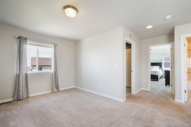 unfurnished bedroom featuring baseboards, light colored carpet, and visible vents