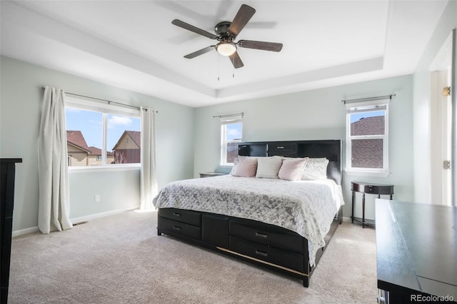 bedroom featuring visible vents, light carpet, baseboards, a tray ceiling, and a ceiling fan