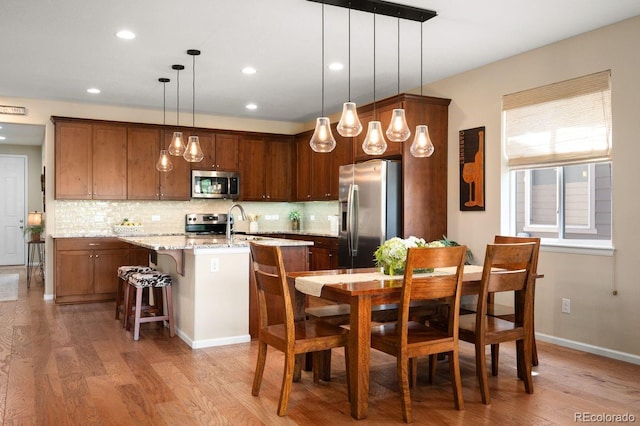 18067 E Anthem Dr, Parker, CO 80134 - kitchen featuring stainless steel appliances, decorative backsplash, light wood-style floors, a kitchen island with sink, and recessed lighting