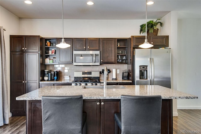 kitchen featuring stainless steel appliances, decorative light fixtures, an island with sink, and dark brown cabinets