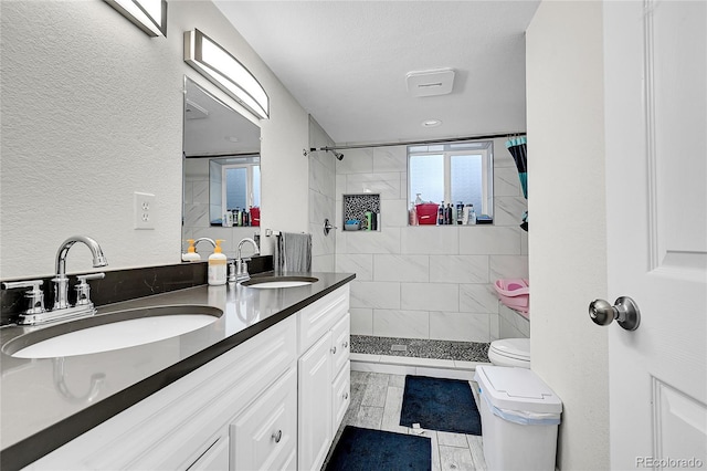 bathroom with a textured ceiling, toilet, vanity, and a tile shower