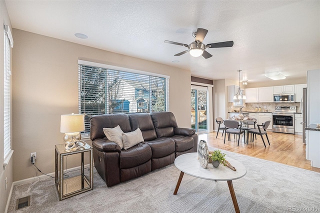 living room featuring ceiling fan, sink, a textured ceiling, and light wood-type flooring