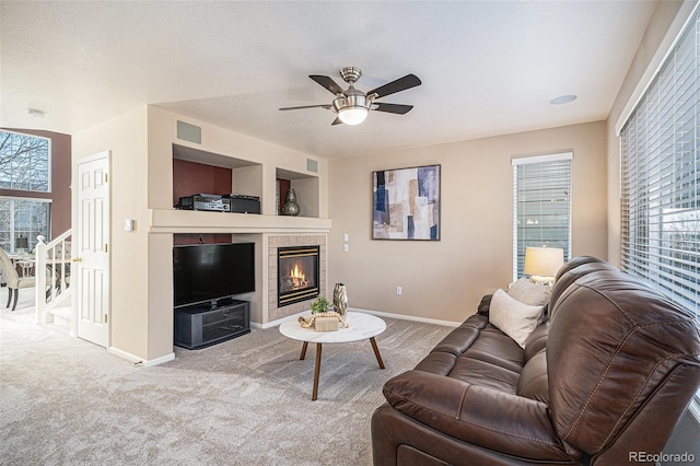 carpeted living room with built in shelves, ceiling fan, a tiled fireplace, and a textured ceiling