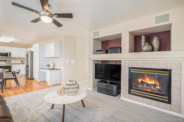 living room featuring a tiled fireplace, ceiling fan, light carpet, and a textured ceiling