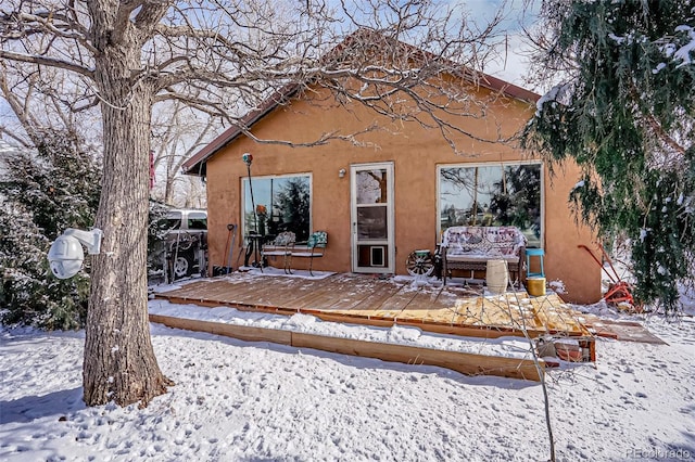 snow covered back of property with an outdoor living space and a deck