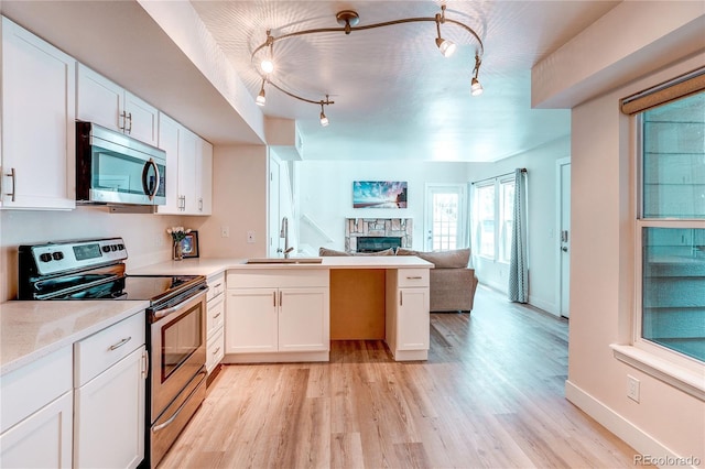 919 S Dawson Way Unit 14, Aurora, CO 80012 - kitchen with appliances with stainless steel finishes, open floor plan, a stone fireplace, a peninsula, and light wood-style floors