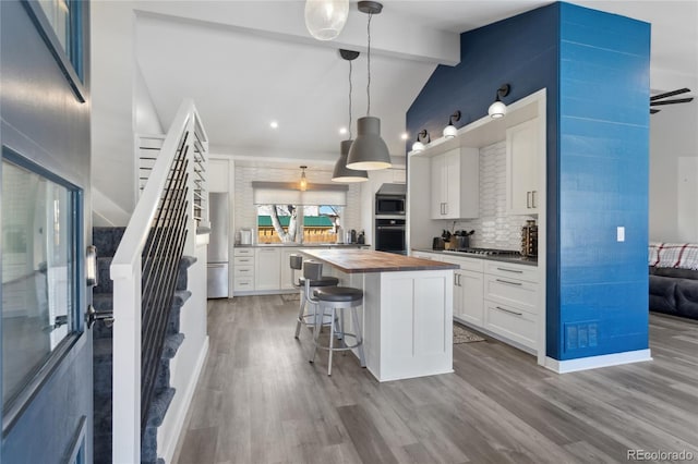 kitchen featuring wooden counters, appliances with stainless steel finishes, white cabinetry, lofted ceiling with beams, and decorative light fixtures