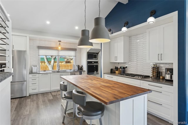 kitchen with a breakfast bar, decorative light fixtures, white cabinets, wooden counters, and stainless steel appliances