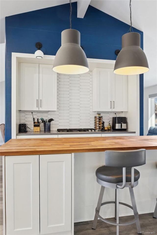 kitchen featuring butcher block countertops, stainless steel gas stovetop, lofted ceiling, backsplash, and hanging light fixtures