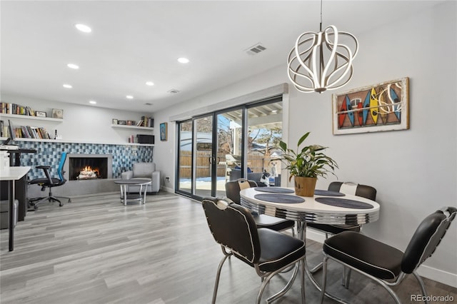 dining room featuring a tile fireplace, an inviting chandelier, and light hardwood / wood-style flooring