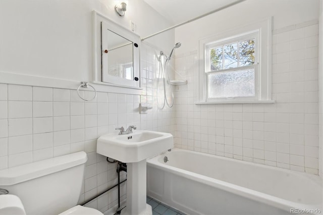 bathroom featuring tiled shower / bath combo, toilet, and tile walls