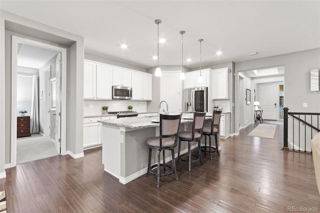 18922 W 84th Ave, Arvada, CO 80007 - kitchen with white cabinets, appliances with stainless steel finishes, a kitchen breakfast bar, dark wood finished floors, and an island with sink