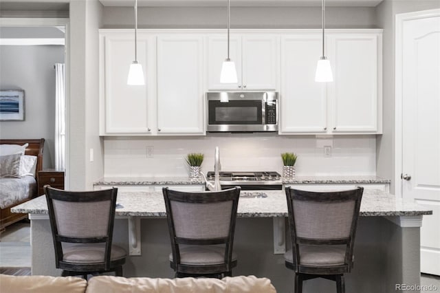 18922 W 84th Ave, Arvada, CO 80007 - kitchen with white cabinets, light stone countertops, stainless steel microwave, decorative light fixtures, and backsplash