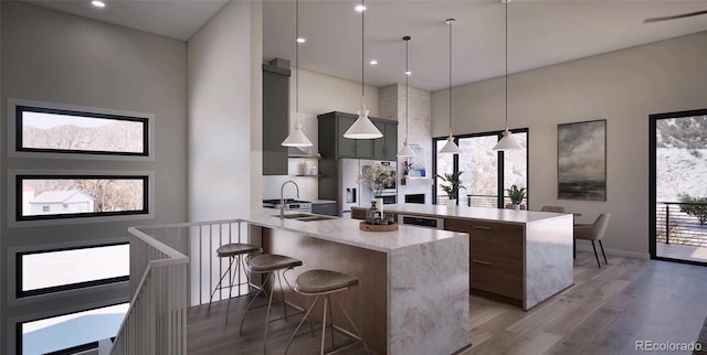 kitchen featuring white refrigerator with ice dispenser, a kitchen breakfast bar, decorative light fixtures, light stone countertops, and wood-type flooring