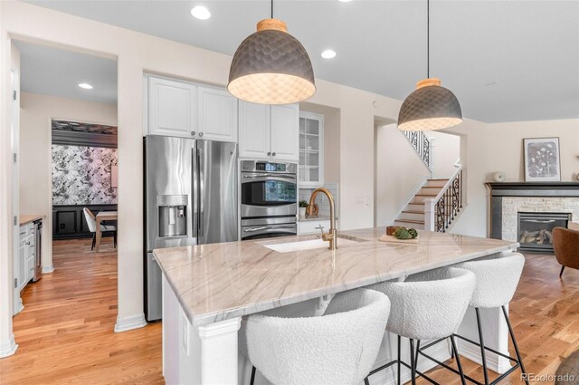 10546 Sundial Rim Rd, Highlands Ranch, CO 80126 - kitchen featuring stainless steel appliances, a sink, light stone countertops, white cabinetry, and light wood-type flooring