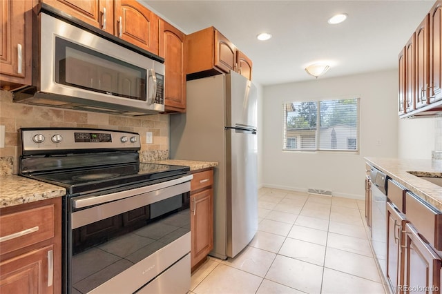4972 W Custer Pl, Denver, CO 80219 - kitchen featuring appliances with stainless steel finishes, backsplash, brown cabinets, recessed lighting, and light tile patterned floors