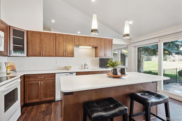 kitchen with white appliances, dark wood-type flooring, hanging light fixtures, a kitchen island, and a kitchen bar