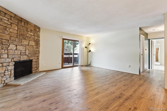 unfurnished living room featuring a stone fireplace, light hardwood / wood-style floors, and a textured ceiling