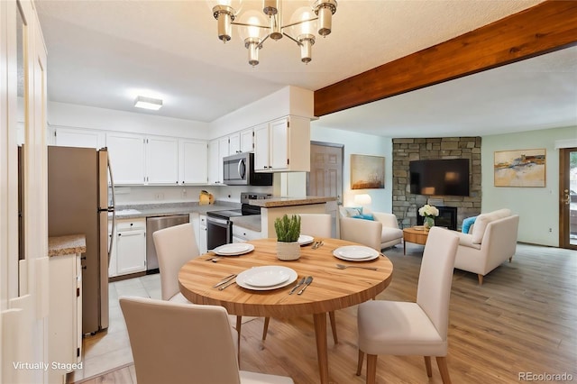 dining space with beamed ceiling, a stone fireplace, an inviting chandelier, and light hardwood / wood-style floors