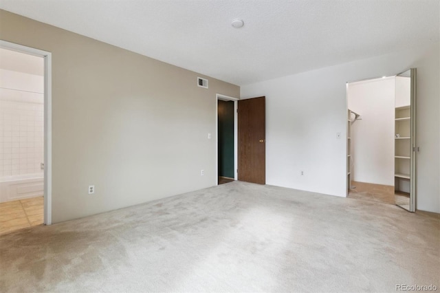 unfurnished bedroom featuring a spacious closet, ensuite bathroom, a textured ceiling, and carpet