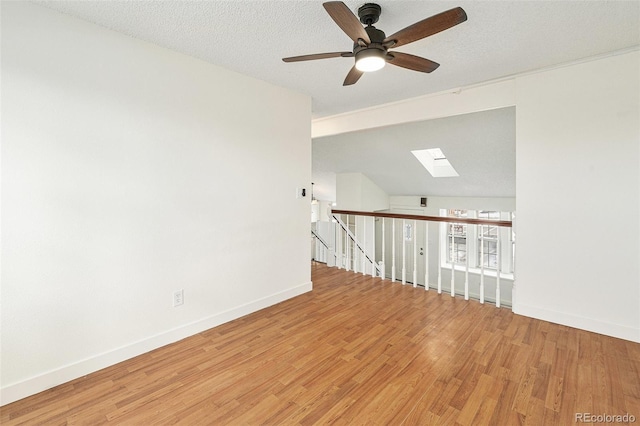 unfurnished room featuring ceiling fan, a skylight, a textured ceiling, and light wood-type flooring