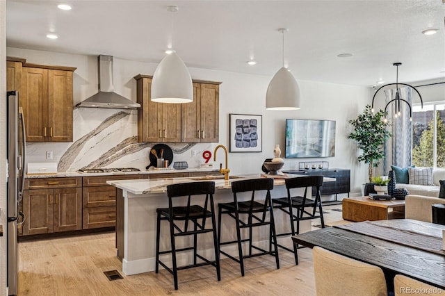 17146 W 92nd Loop, Arvada, CO 80007 - kitchen featuring wall chimney exhaust hood, a sink, light wood finished floors, open floor plan, and a kitchen breakfast bar