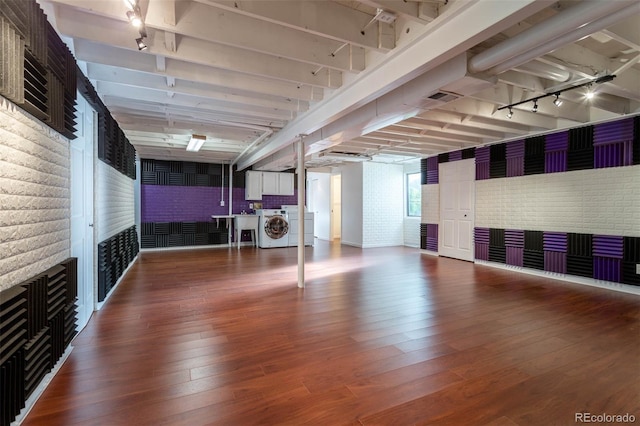 basement with washer / dryer, hardwood / wood-style floors, brick wall, and track lighting