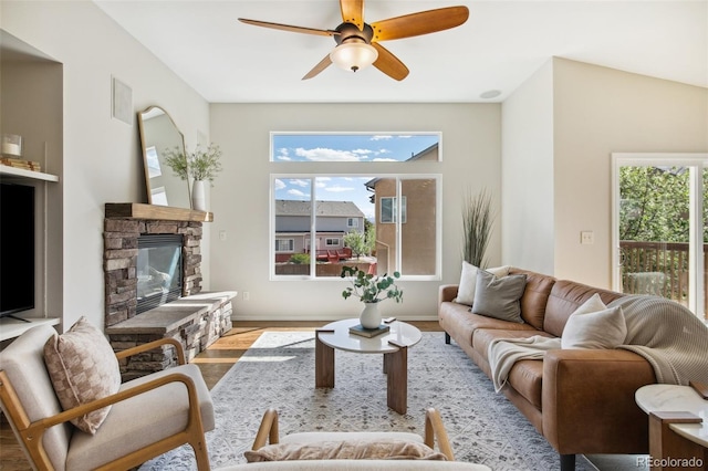 living area with plenty of natural light, wood finished floors, a ceiling fan, and a stone fireplace