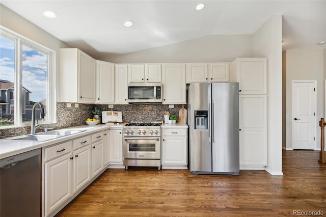 kitchen featuring appliances with stainless steel finishes, a sink, lofted ceiling, backsplash, and white cabinets