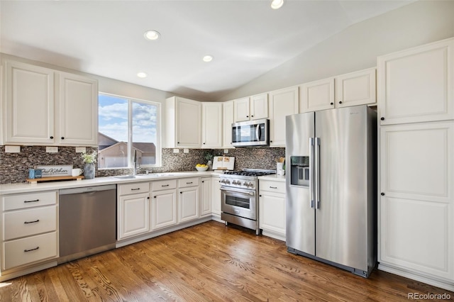 kitchen featuring stainless steel appliances, a sink, lofted ceiling, decorative backsplash, and white cabinets