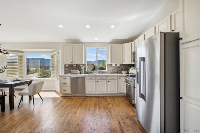 kitchen with appliances with stainless steel finishes, light wood-style flooring, decorative backsplash, a sink, and white cabinets
