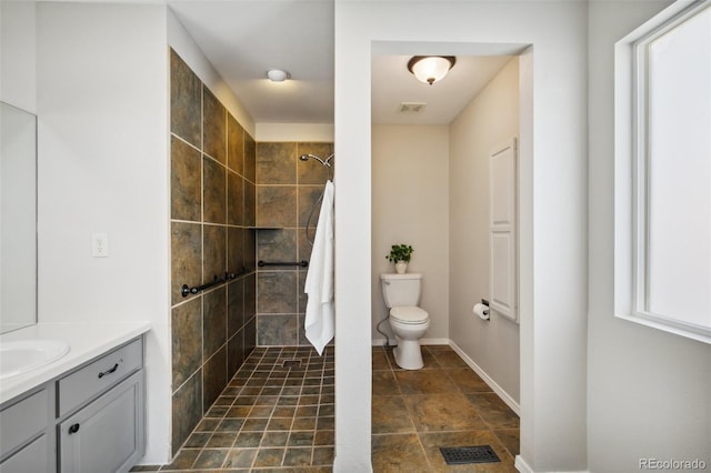 full bathroom featuring a tile shower, toilet, vanity, and baseboards