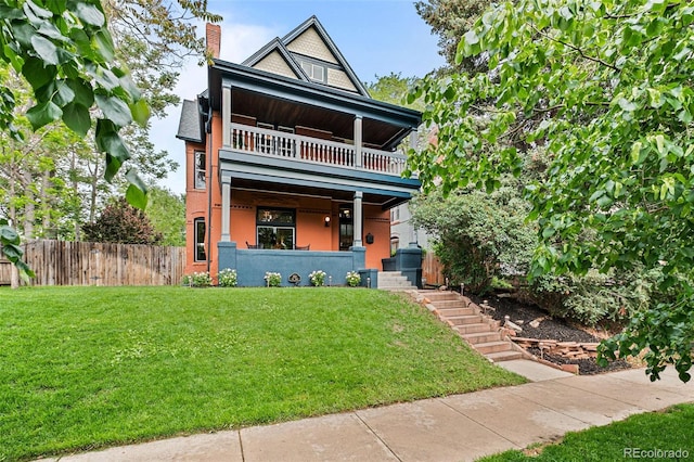 view of front of property with a front yard, a balcony, fence, and a chimney