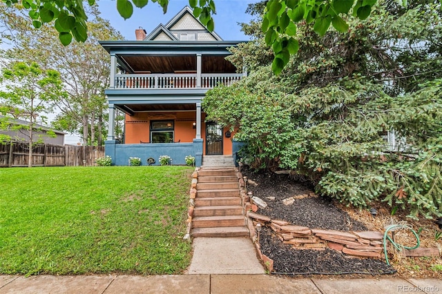 view of front of house with a front yard, a balcony, fence, and a chimney