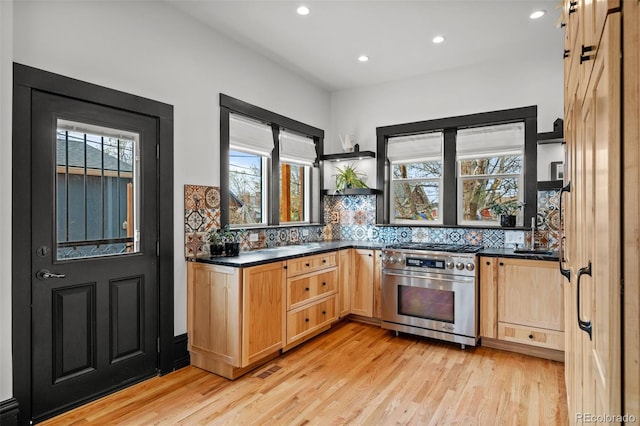 kitchen with light wood-style floors, open shelves, dark countertops, stainless steel gas range oven, and backsplash