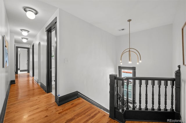 hallway with light wood-type flooring, visible vents, baseboards, and an upstairs landing