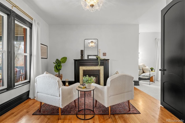 living area with a stone fireplace, an inviting chandelier, wood finished floors, and baseboards